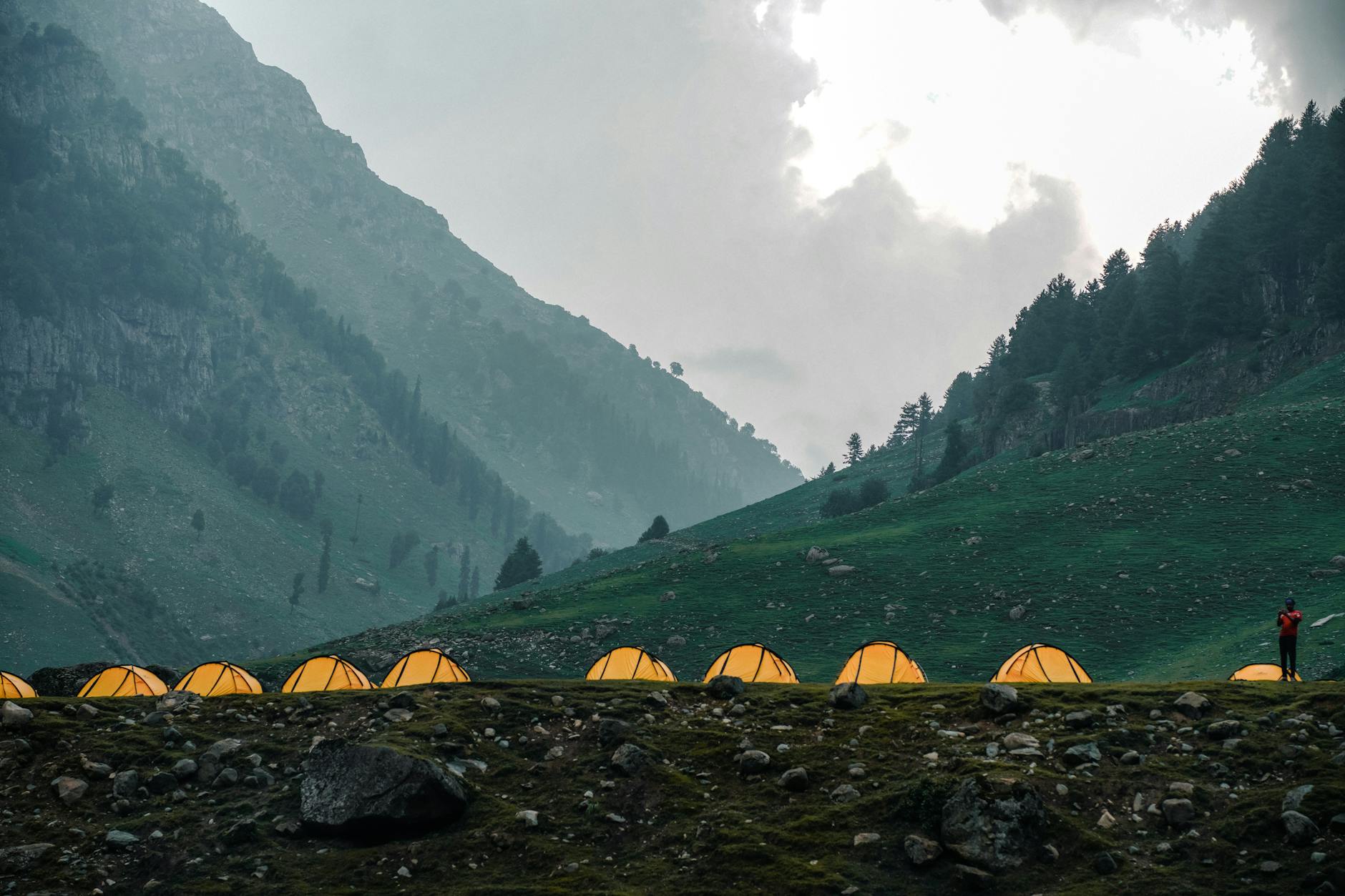 Nocny obóz w górach z oświetlonymi namiotami i samotnym wędrowcem