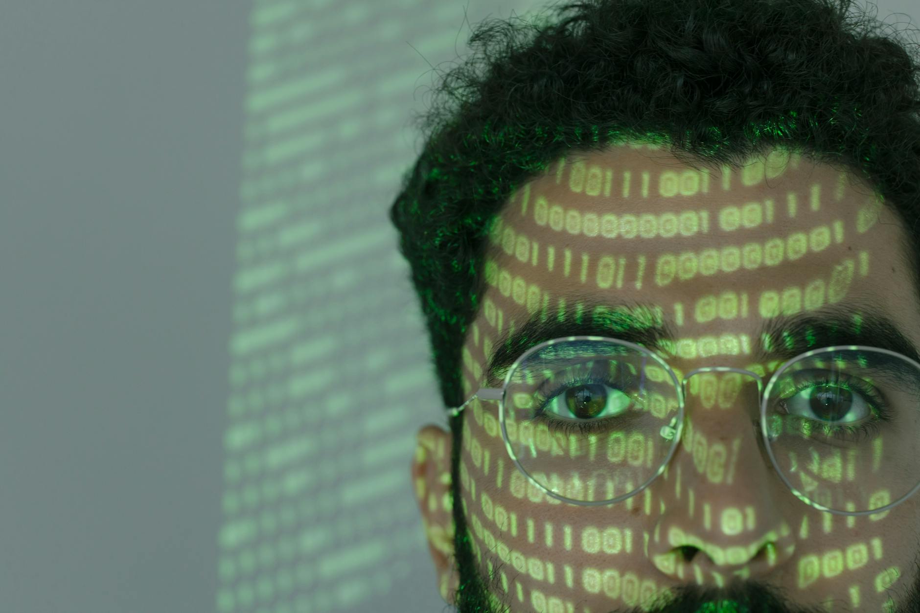 Mężczyzna z twarzą oświetloną kodem binarnym symbolizującym cyberatak