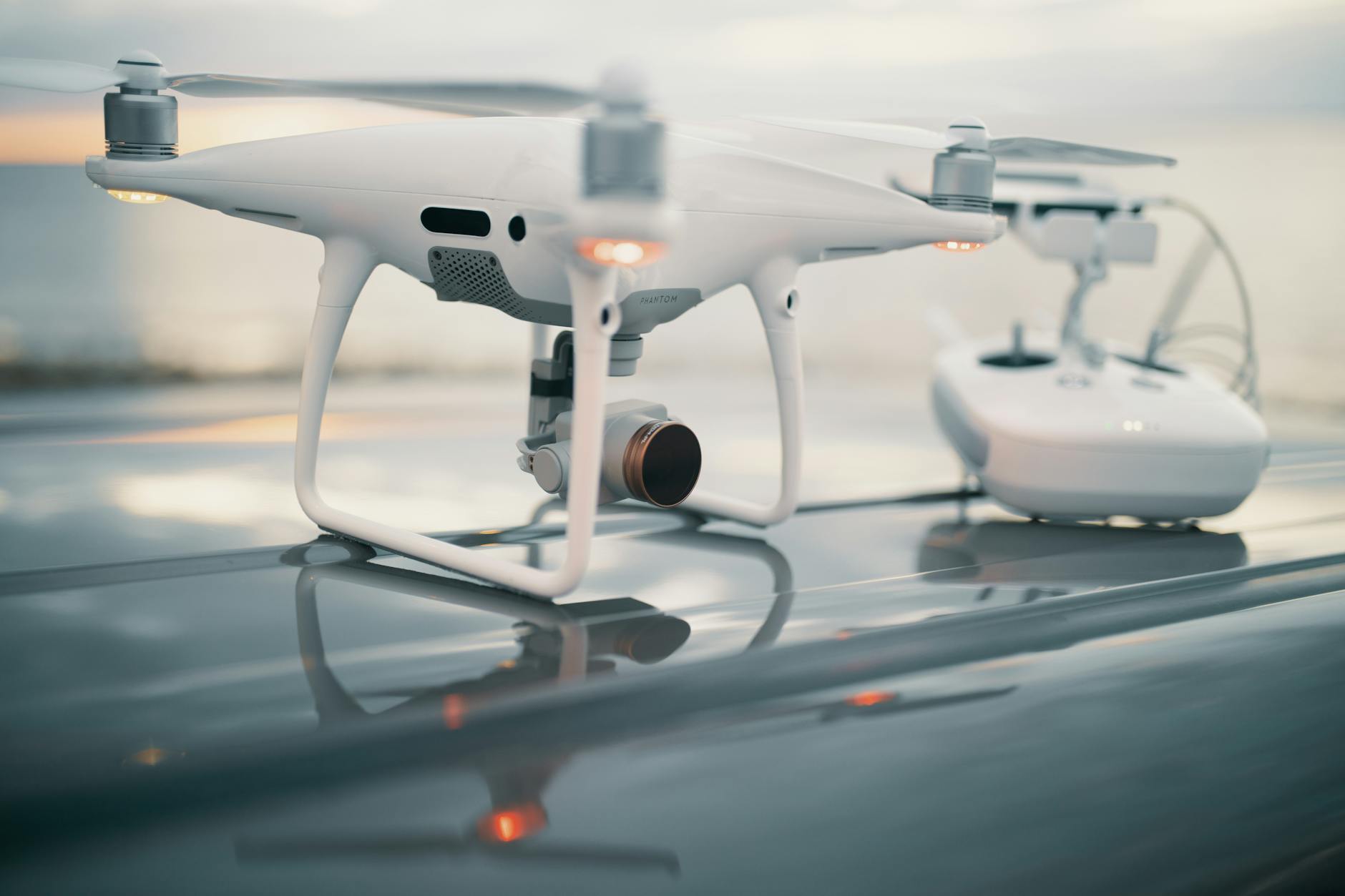 Nowoczesny dron z kontrolerem na lśniącej powierzchni o zachodzie słońca
