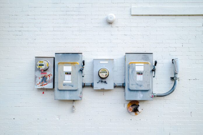 Skrzynki elektryczne i liczniki prądu na białej ceglanej ścianie Skrzynki elektryczne i liczniki prądu na białej ceglanej ścianie